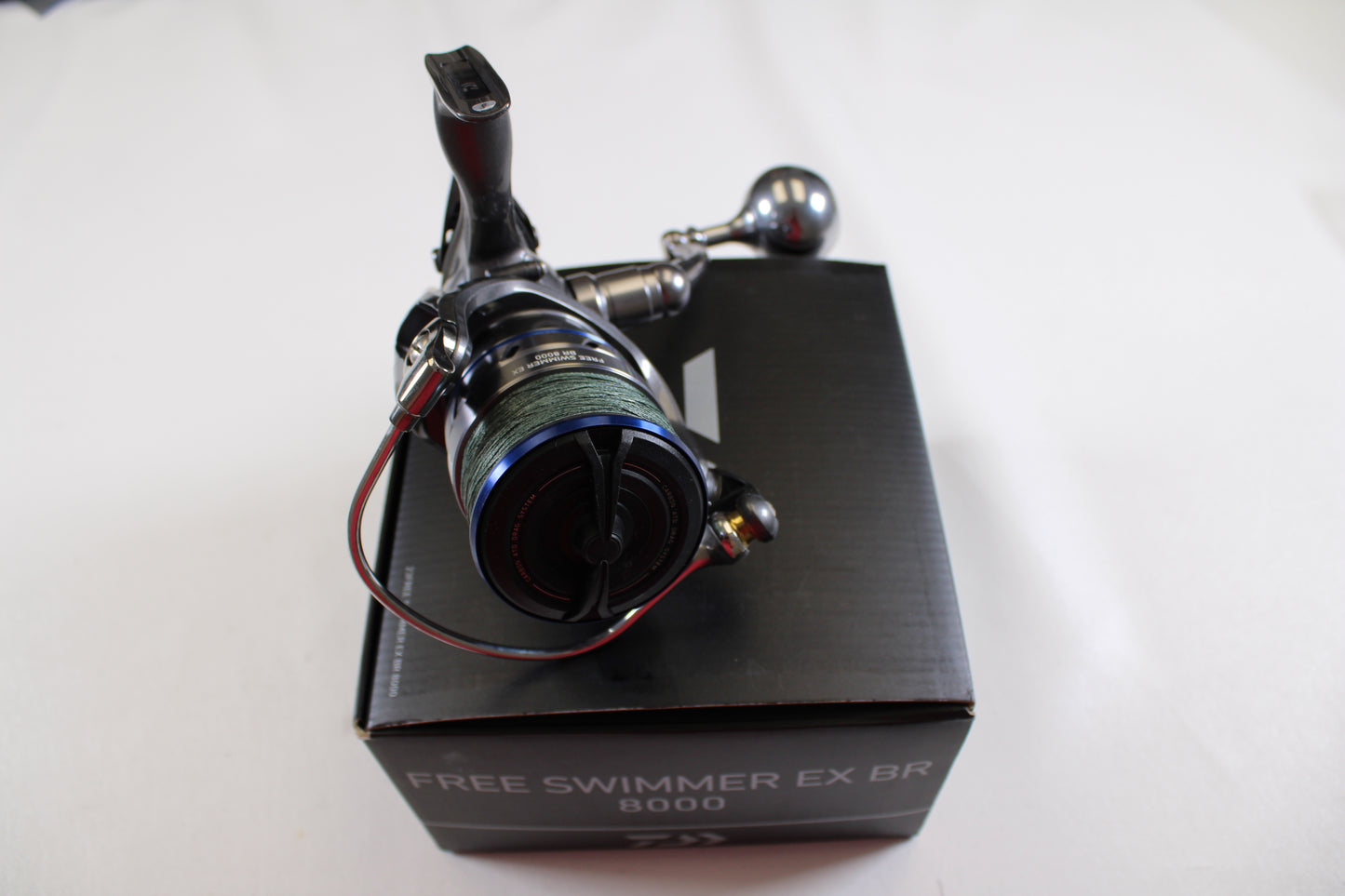 A Daiwa Free Swimmer EX BR 8000 used spinning reel in excellent condition, featuring blue and black accents, is shown on a black box. Trade in your old fishing gear for store credit with our Rod and Reel Trade-In Program. Background: plain white.