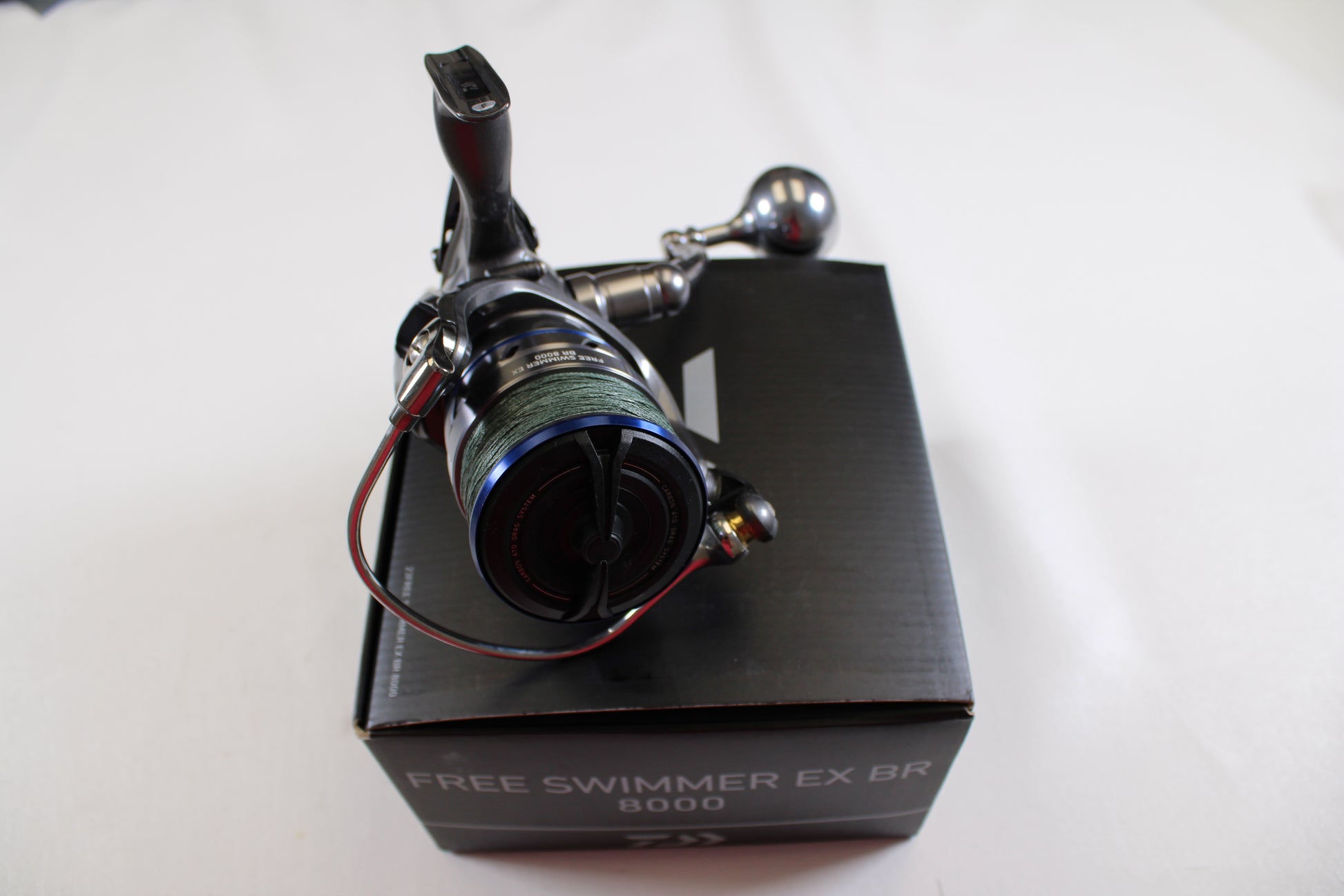 A Daiwa Free Swimmer EX BR 8000 used spinning reel in excellent condition, featuring blue and black accents, is shown on a black box. Trade in your old fishing gear for store credit with our Rod and Reel Trade-In Program. Background: plain white.
