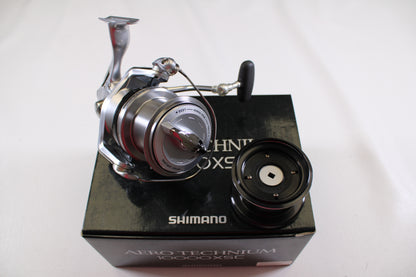 A Shimano Aero Technium 10000XSC used spinning reel in excellent condition is shown with its original black box and an extra spool on a white background.