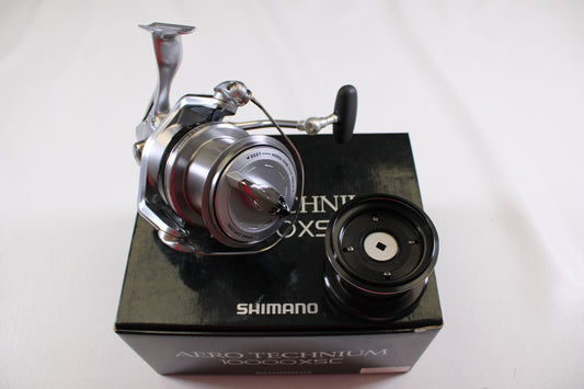 A Shimano Aero Technium 10000XSC used spinning reel in excellent condition is shown with its original black box and an extra spool on a white background.