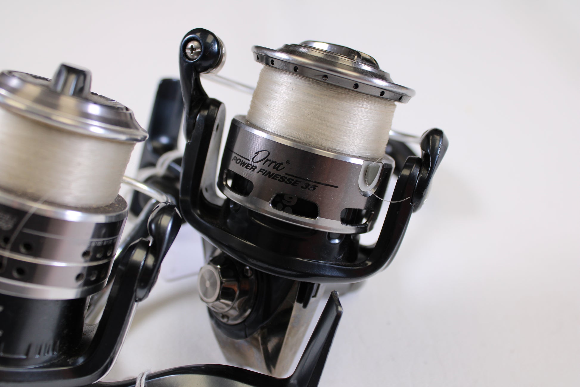 Close-up of two used Abu Garcia spinning reels, Orra Power Finesse 35 and Cardinal STX20 (both in good condition), with white fishing line on a plain white background—ideal for trade-in or store credit upgrades.