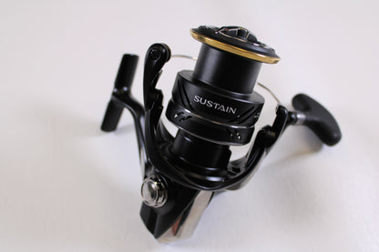 A close-up of the Shimano Sustain FJ SA4000XGFJ 6.2:1 Spinning Reel in Mint Used Condition, featuring metallic and gold accents with a visible spool and handle—perfect for Rod and Reel Trade-In or store credit.
