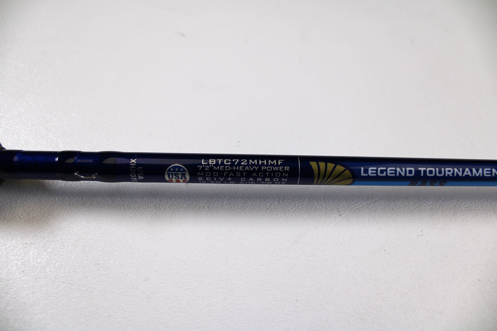 A close-up of a St. Croix Legend Tournament Bass LBTC72MHMF Finesse Carbon Cranker 7'2" Medium Heavy Used Casting Rod in excellent condition, with a USA flag emblem and Rod & Reel Trade-In Program details on metallic blue.