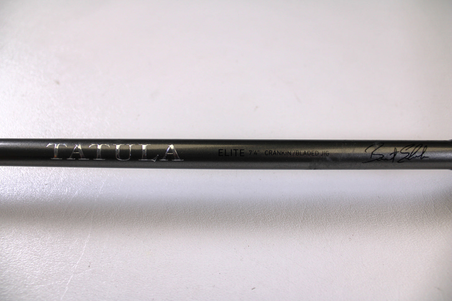 A close-up of the Daiwa Tatula Elite TTEL741MHRB-G 7'4" Medium Heavy Used Casting Rod in very good condition, featuring "TATULA ELITE 7'4" CRANK/BLADED JIG" text and a signature on a black rod—ideal for our Rod and Reel Trade-In Program.