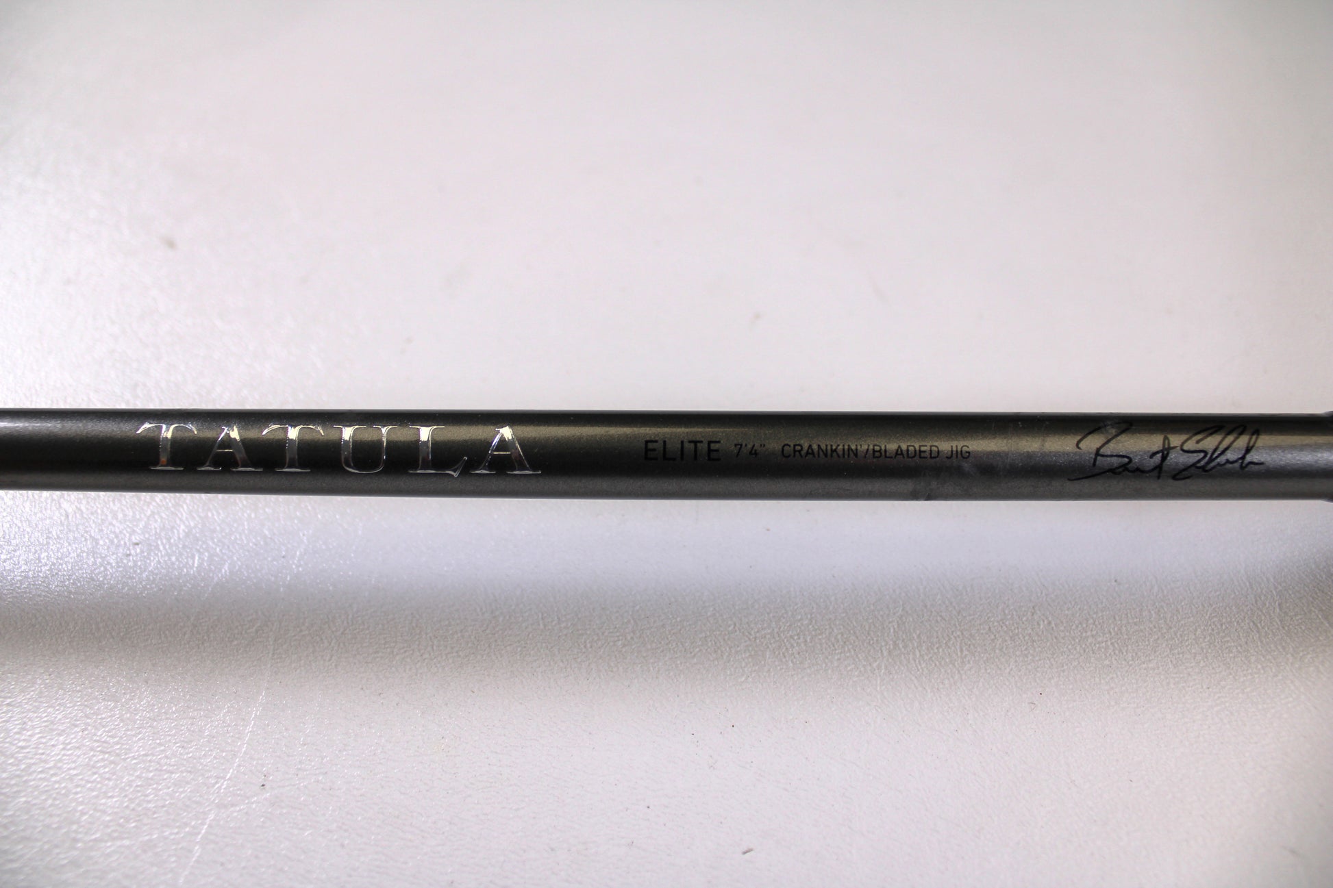 A close-up of the Daiwa Tatula Elite TTEL741MHRB-G 7'4" Medium Heavy Used Casting Rod in very good condition, featuring "TATULA ELITE 7'4" CRANK/BLADED JIG" text and a signature on a black rod—ideal for our Rod and Reel Trade-In Program.