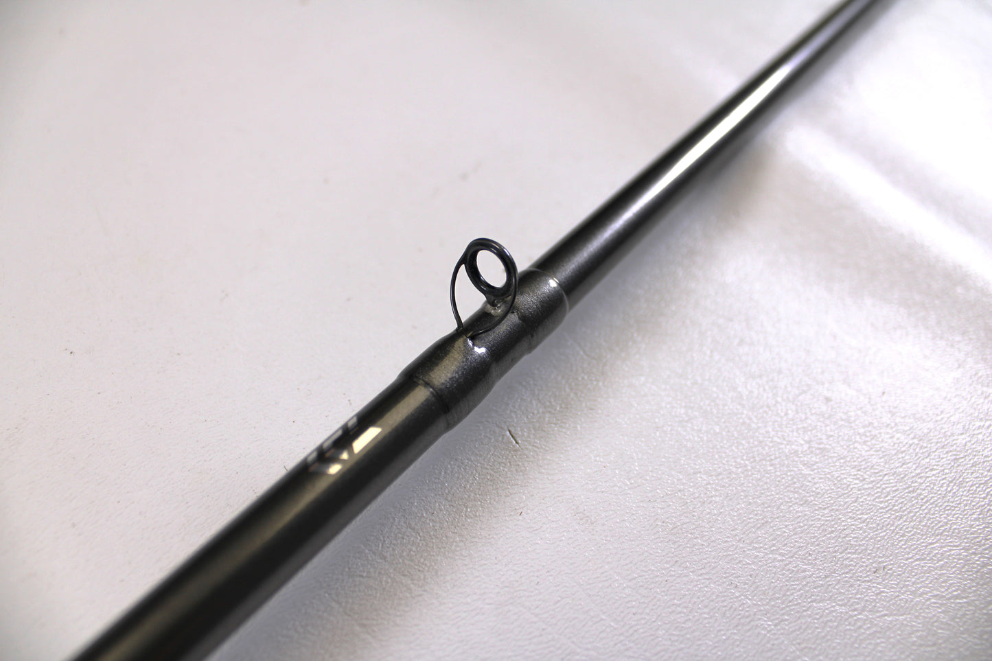 A close-up of a Daiwa Tatula Elite TTEL741MHRB-G 7'4" Medium Heavy Used Casting Rod in very good condition, focusing on a line guide against a plain, light background.