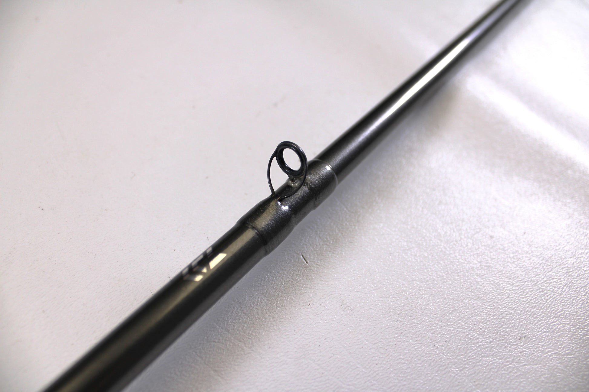 A close-up of a Daiwa Tatula Elite TTEL741MHRB-G 7'4" Medium Heavy Used Casting Rod in very good condition, focusing on a line guide against a plain, light background.