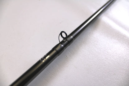 A close-up of a Daiwa Tatula Elite TTEL741MHRB-G 7'4" Medium Heavy Used Casting Rod in very good condition, focusing on a line guide against a plain, light background.