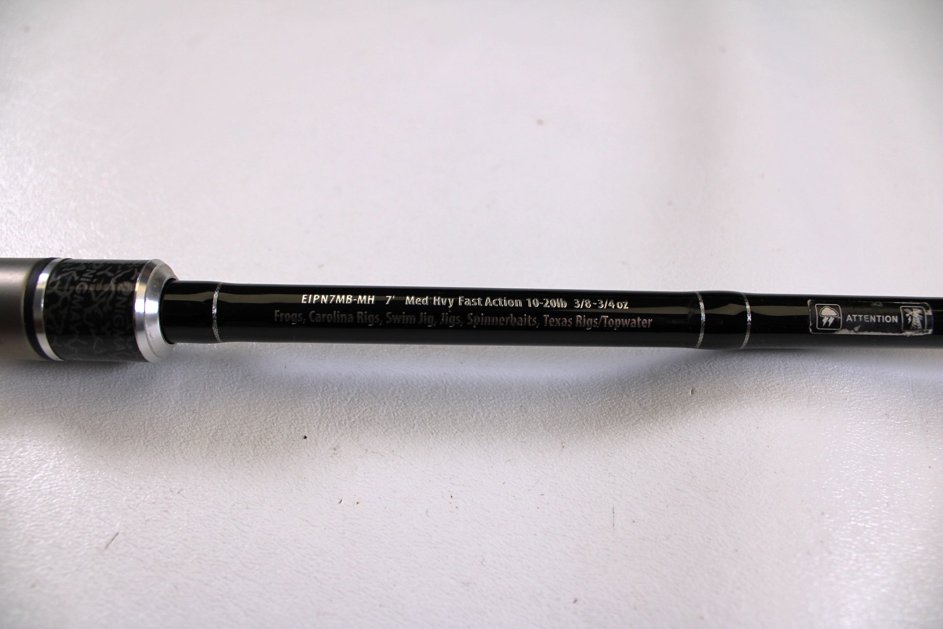 A close-up of the Enigma Ippon EIPN7MB-MH 7'0" Medium Heavy Used Casting Rod in excellent condition, featuring silver accents and detailed specs—trade in your old gear for store credit through the Nation's Best Rod and Reel Trade-In Program.