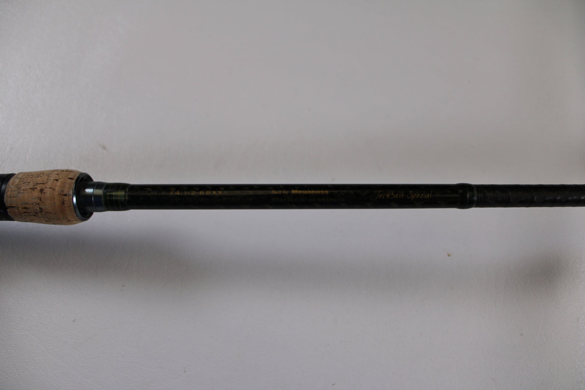 A close-up of the Megabass Orochi XX Aaron Martens F4.1/2-68XX Jerkbait Special casting rod handle (used, fair condition) with a cork grip and black shaft—ideal for trading in used gear during our Rod and Reel Trade-In event.