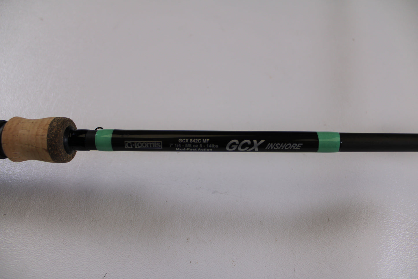 A close-up of the G. Loomis GCX Inshore 842C MF Used Casting Rod in excellent condition shows its label and specifications on the black shaft with a cork handle—eligible for our Rod and Reel Trade-In Program for store credit or used gear upgrades.