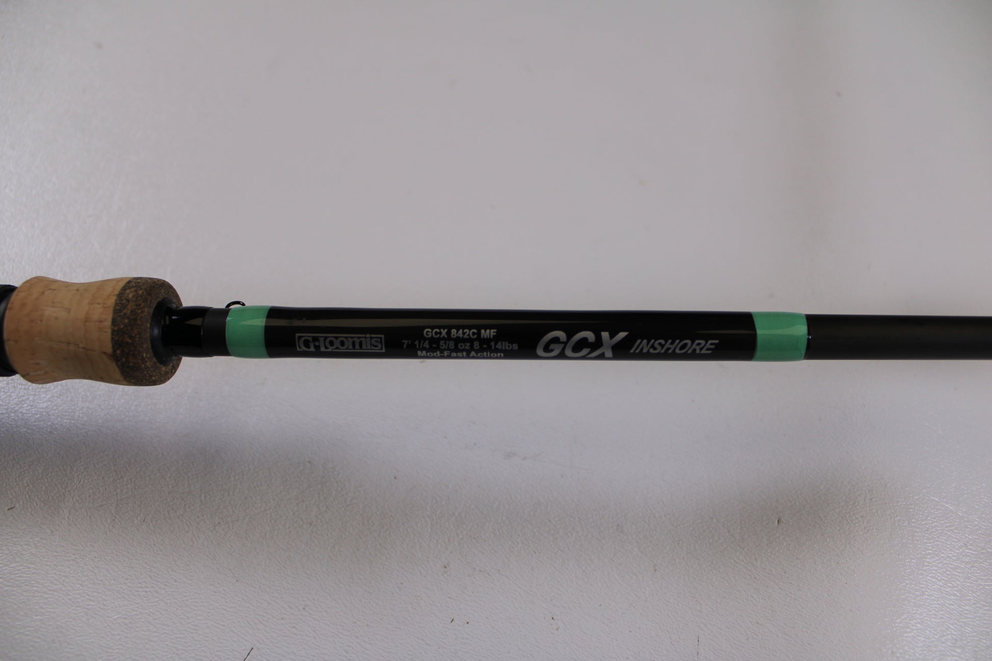 A close-up of the G. Loomis GCX Inshore 842C MF Used Casting Rod in excellent condition shows its label and specifications on the black shaft with a cork handle—eligible for our Rod and Reel Trade-In Program for store credit or used gear upgrades.