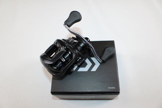A Daiwa Tatula 200 TAT200HL Used Casting Reel in excellent condition rests on a black Daiwa box—ideal for earning store credit or upgrading gear with our Rod and Reel Trade-In program.