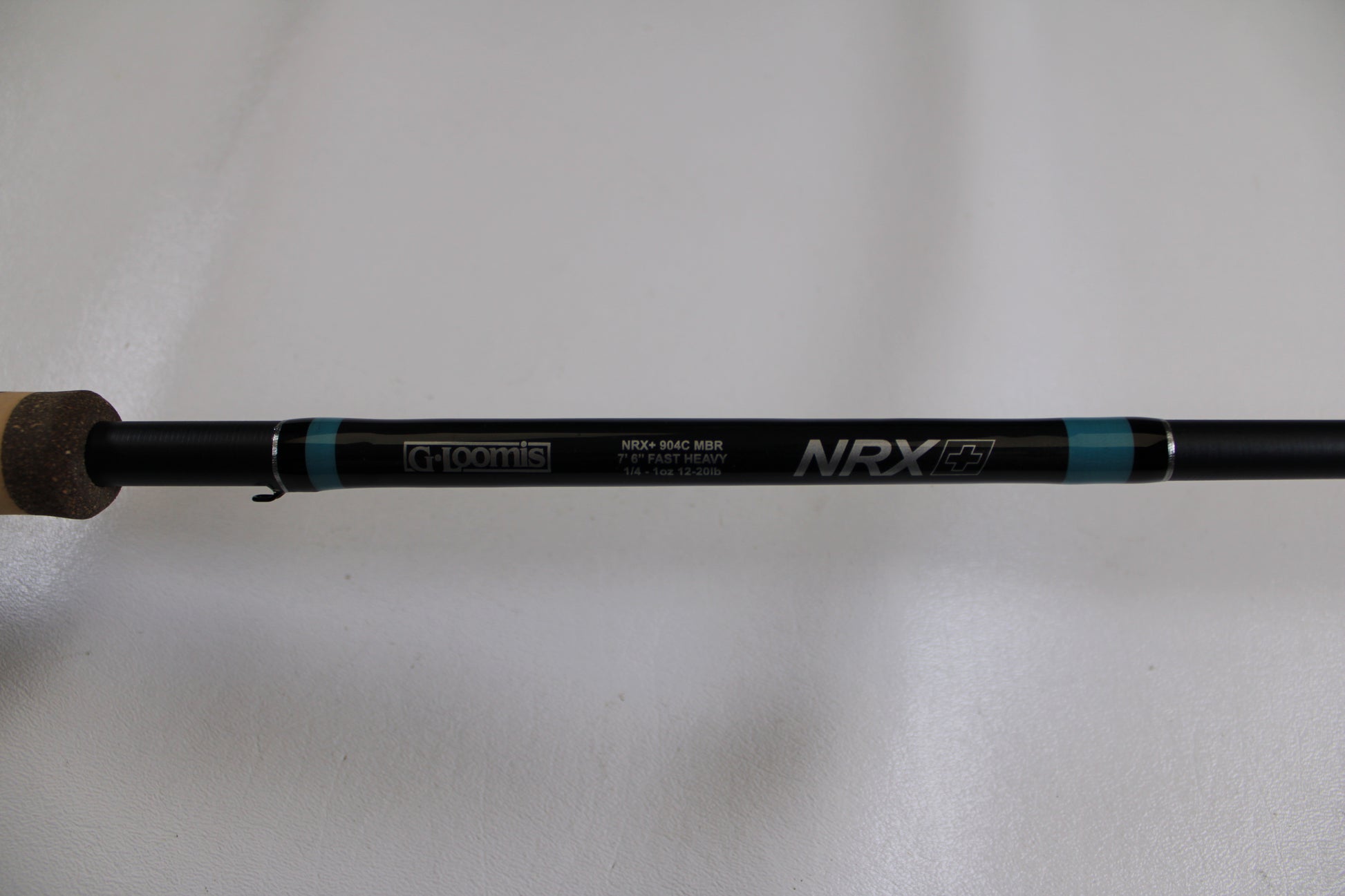 A close-up of a G. Loomis NRX+ 904C MBR Used Casting Rod in excellent condition, showing cork handle and brand logos on the black rod against a plain white background.