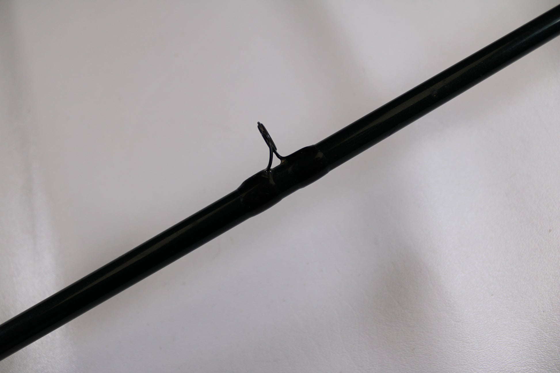A close-up of the G. Loomis FGR863 7'2" Medium Heavy Used Casting Rod's dark green guide with metal loop, set against a white background—ideal for anyone exploring our rod and reel trade-in program.