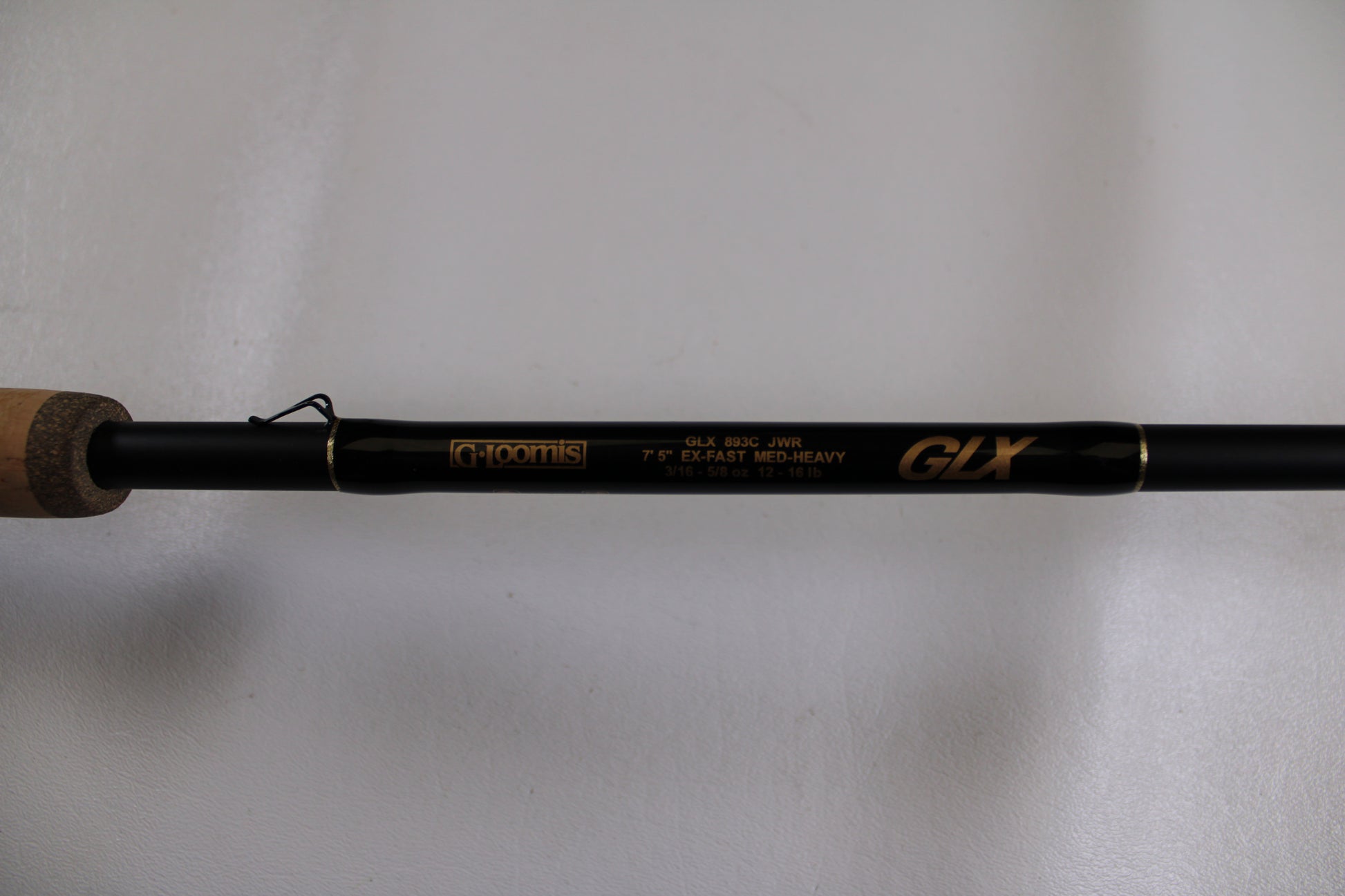 A close-up of a G. Loomis GLX 893c JWR 7'5" Medium Heavy used casting rod in excellent condition, featuring gold text on a black rod and a partially visible cork handle—ideal for Rod and Reel Trade-In or earning store credit.
