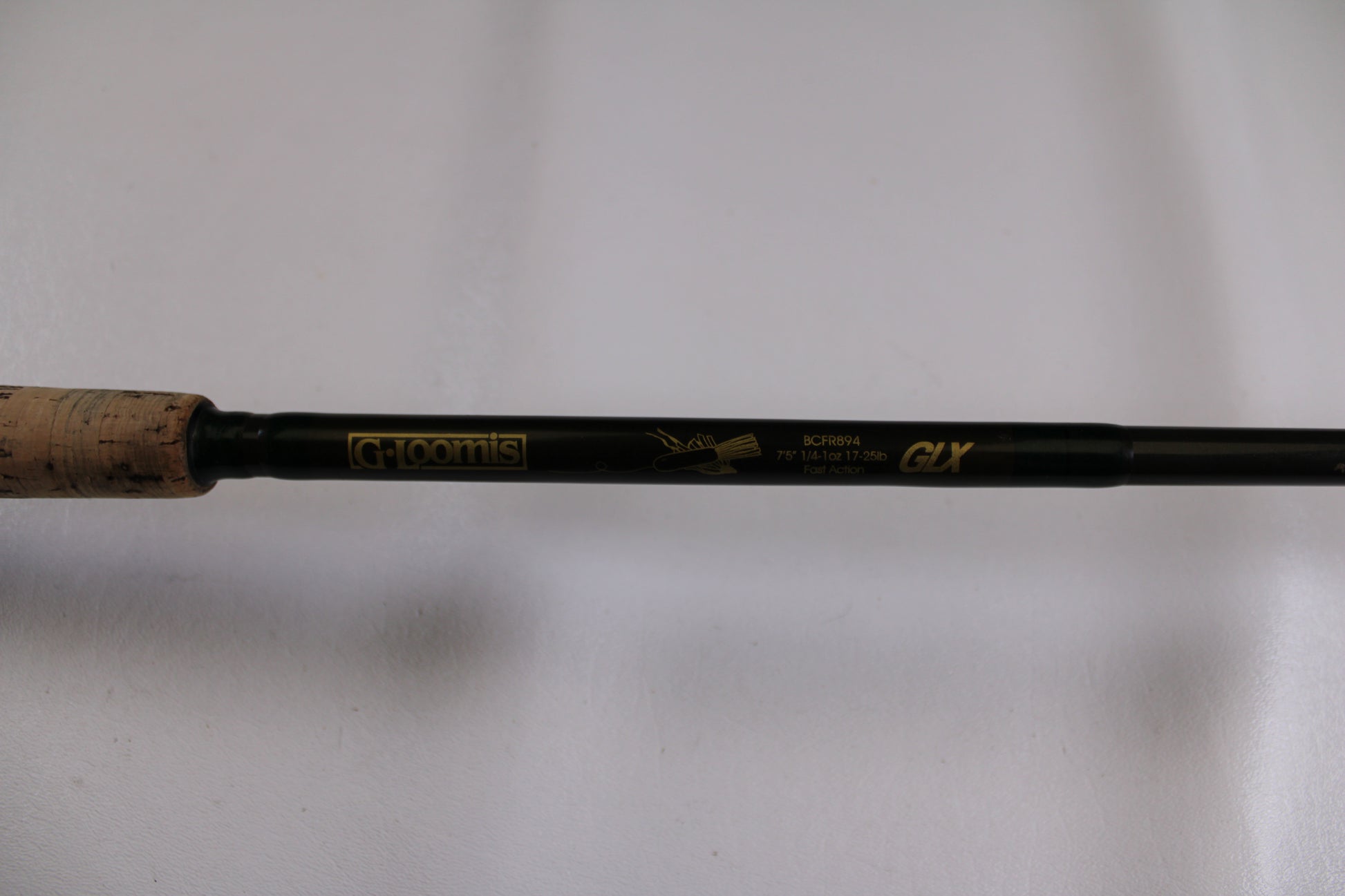 Close-up of the G. Loomis BCFR894 GLX used casting rod in good condition, featuring gold model details on a dark shaft with cork grip—ideal for upgrading your gear through our rod and reel trade-in program for store credit.