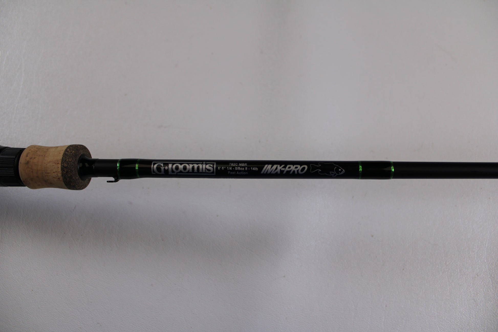 A close-up of the G. Loomis IMX-PRO 782c MBR 6'6" Medium Used Casting Rod in excellent condition shows the brand and model on its black rod with green accents and a cork handle—ideal for Rod and Reel Trade-In or checking used gear.