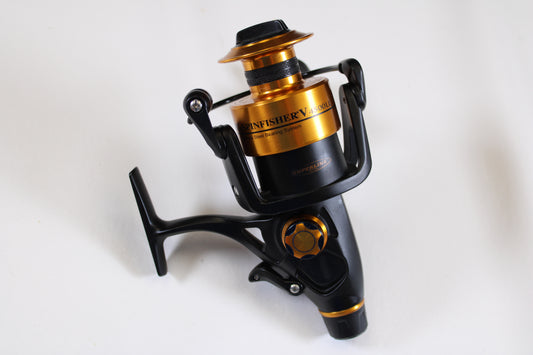 A close-up of a Penn Spinfisher V 4500 SSV4500LL Used Spinning Reel in black and gold, possibly eligible for our Rod and Reel Trade-In Program, rests on a white surface.