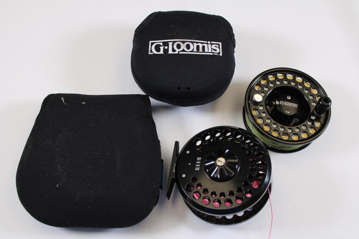 Two G. Loomis GL 8-9-10 fly reels with spare spool in excellent used condition are shown next to their branded black cases—ideal gear for our Rod and Reel Trade-In Program.