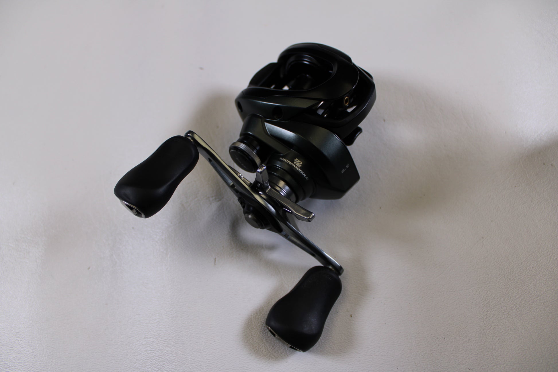 A Shimano Curado CUMGL150 used casting reel in excellent condition with two ergonomic handles is displayed on a plain white surface.
