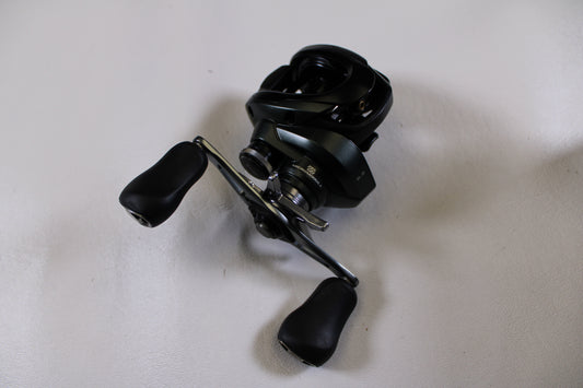 A Shimano Curado CUMGL150 used casting reel in excellent condition with two ergonomic handles is displayed on a plain white surface.