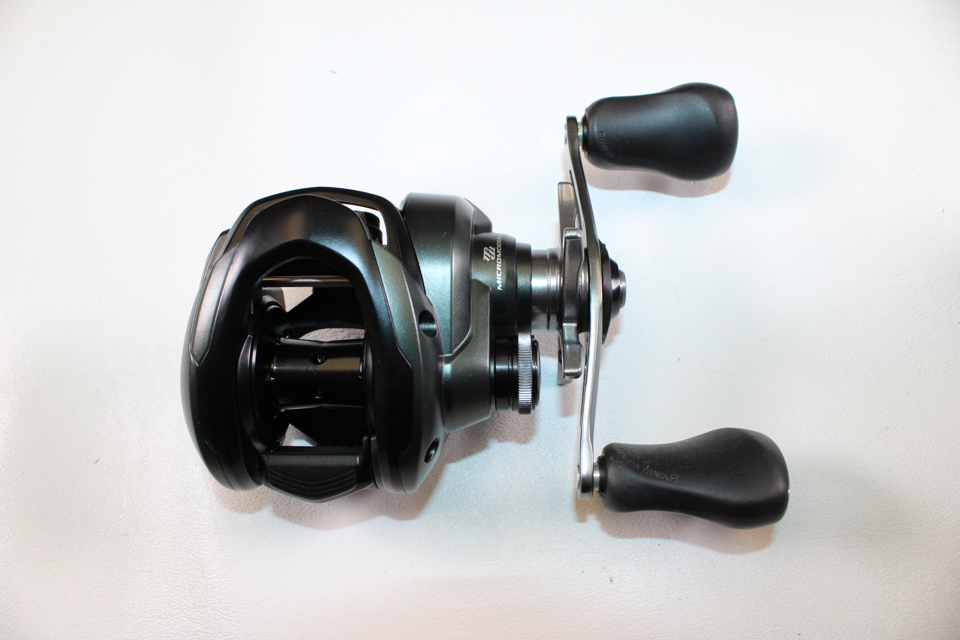 A Shimano Curado CUMGL150 Used Casting Reel by Shimano, in excellent condition with a black and silver finish and two ergonomic handles, displayed on a white surface.