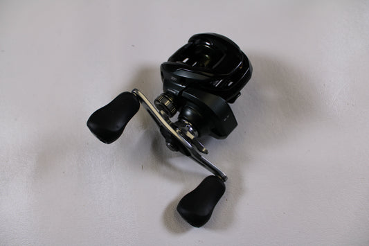 A Shimano Curado 200M 6.2:1 used casting reel in excellent condition with two black rubberized handles is displayed on a white surface—ideal for those interested in used gear or joining our Rod and Reel Trade-In Program.