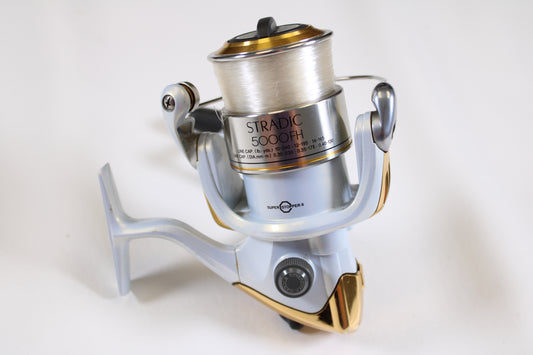 A close-up of a Shimano Stradic 5000FH Used Spinning Reel in very good condition, featuring silver and gold colors with fishing line, set on a plain white background—ideal for our rod and reel trade-in program if you want to upgrade.