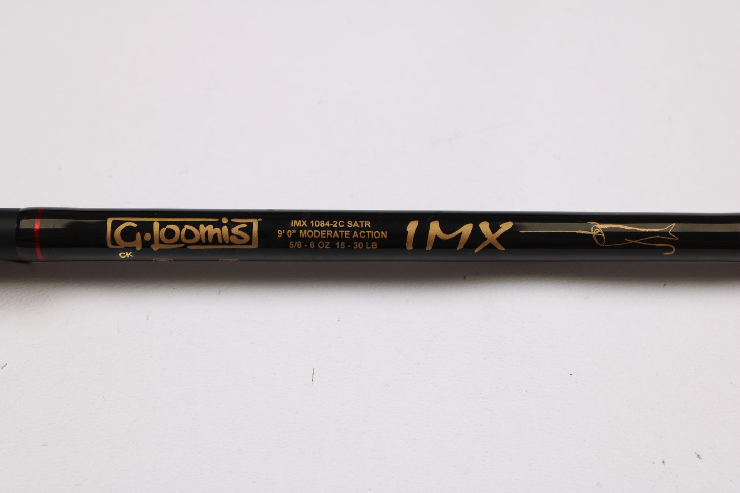 A close-up of a black G. Loomis Salmon & Steelhead IMX 1084-2C SATR 9'0" used casting rod in excellent condition, ideal for gear enthusiasts or trade-ins. The label displays the gold specs and fish outline graphic.
