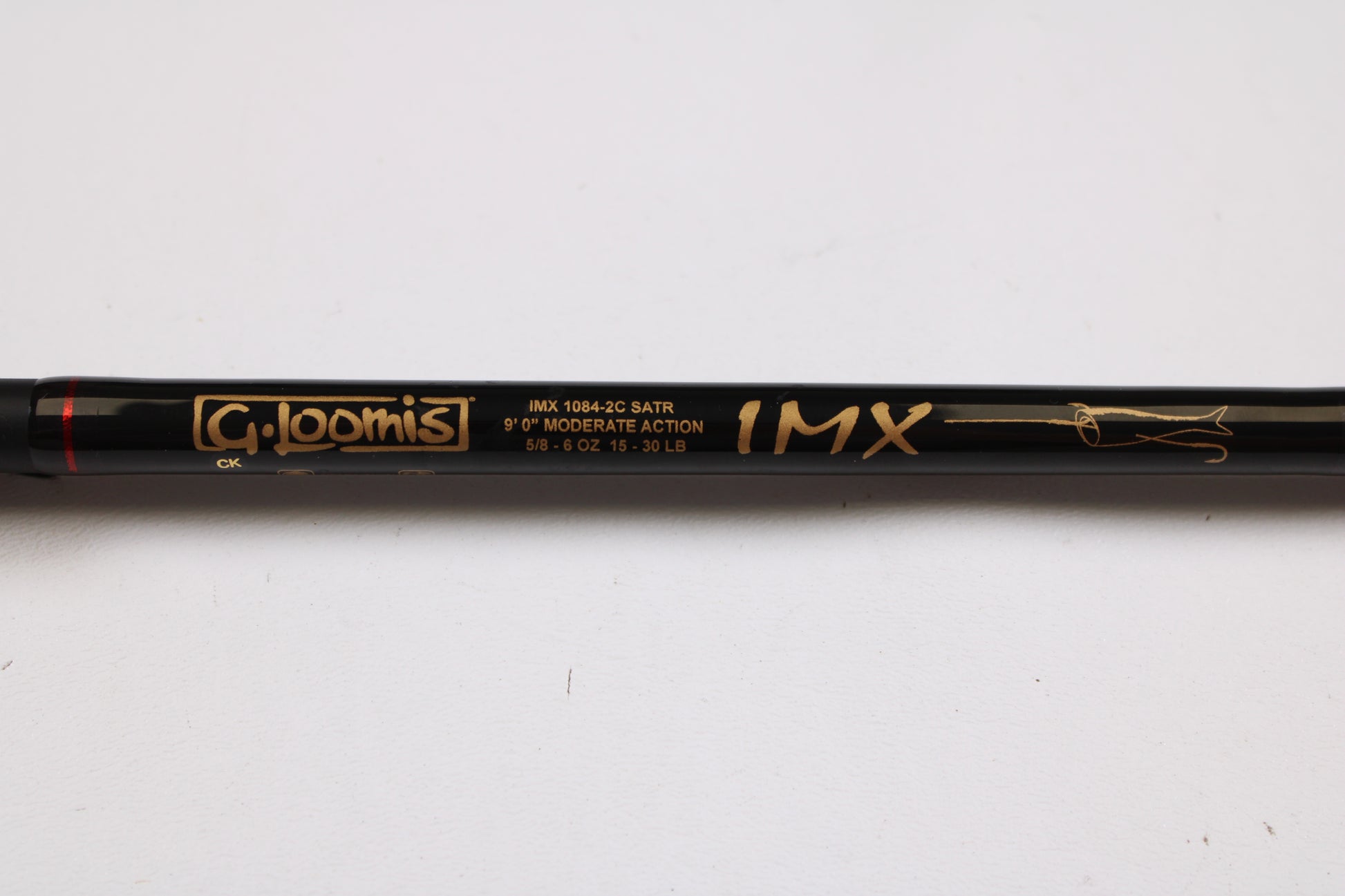 A close-up of a black G. Loomis Salmon & Steelhead IMX 1084-2C SATR 9'0" used casting rod in excellent condition, ideal for gear enthusiasts or trade-ins. The label displays the gold specs and fish outline graphic.