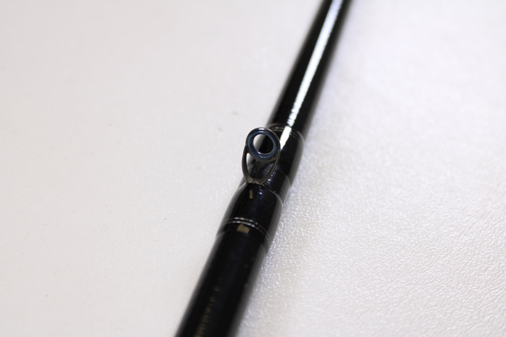 Close-up of a Daiwa Tatula TTU741HRB-G 7'4" Heavy Glass used casting rod in very good condition, featuring a single guide ring on a white surface—perfect for those interested in quality used gear or our Rod and Reel Trade-In Program.