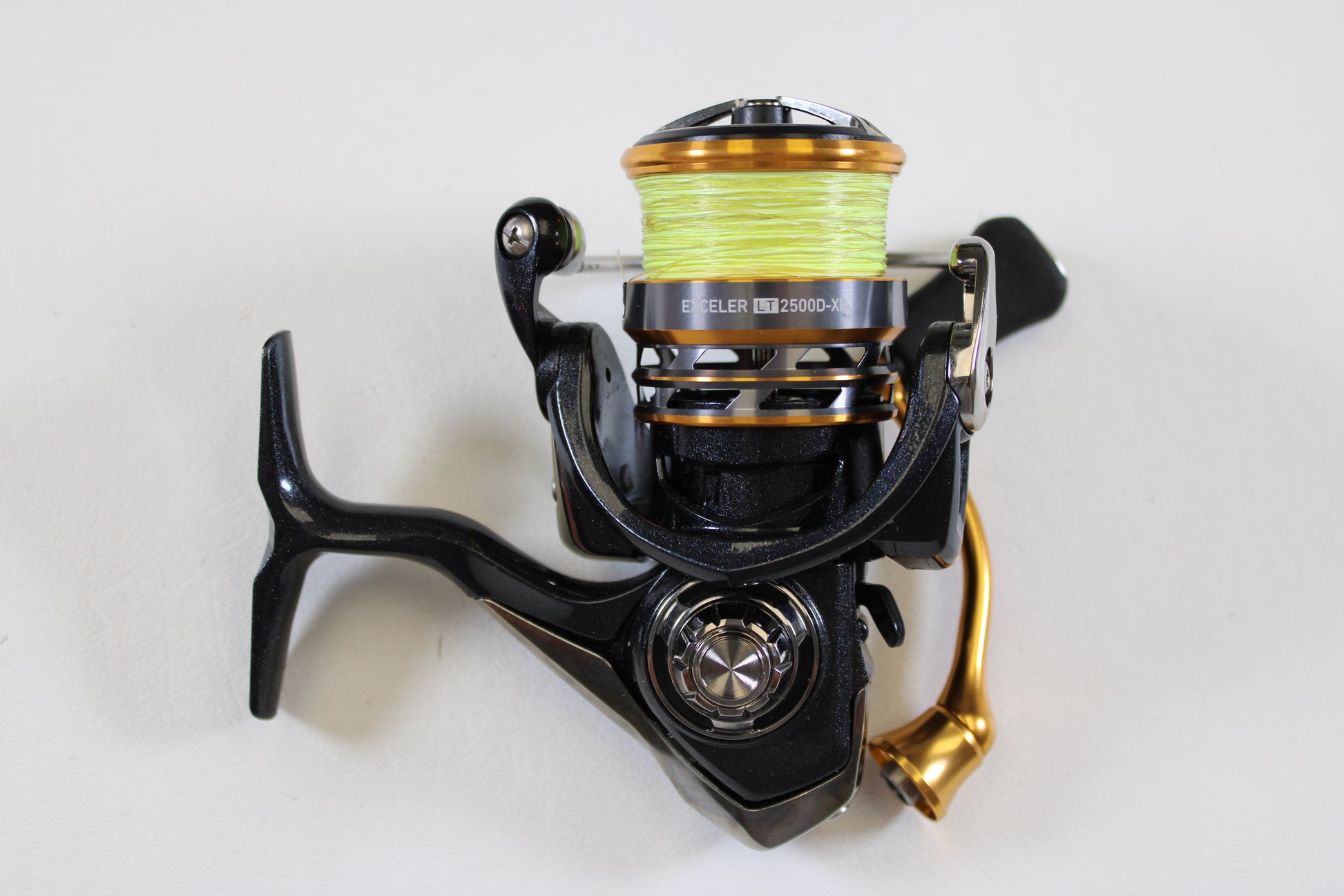 A close-up of a Daiwa Exceler LT EXLT2500D-XH 6.2:1 Used Spinning Reel in excellent condition, featuring black and gold accents with yellow line—ideal for our Rod and Reel Trade-In Program. Shown against a plain white background.