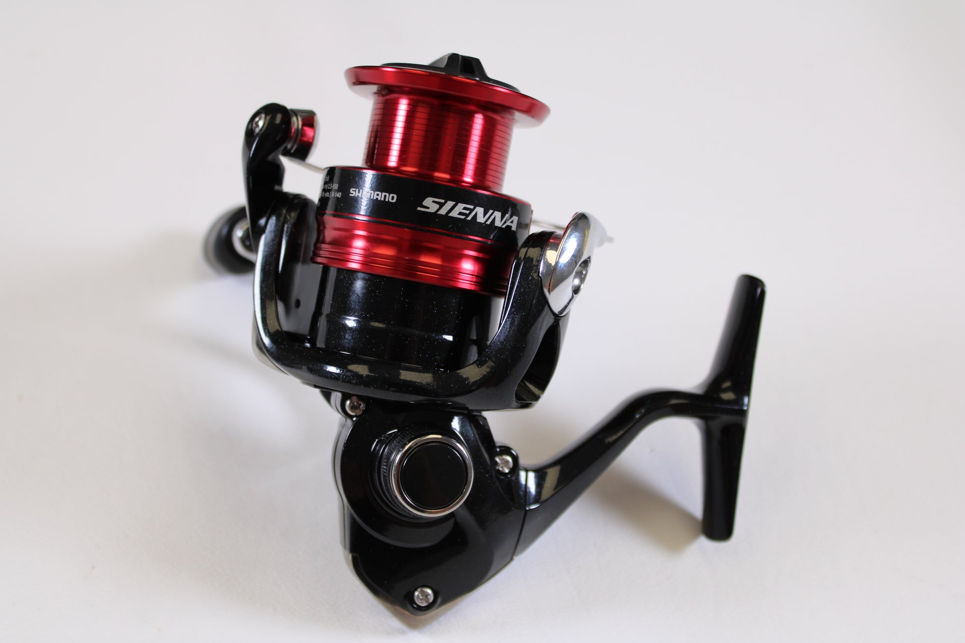A close-up of the Shimano Sienna FG SN2500HGFG used spinning reel in excellent condition features a sleek black body and red spool, displayed on a white background—ideal for those exploring rod and reel trade-in options for store credit.