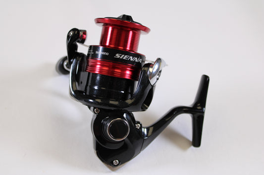 A close-up of the Shimano Sienna FG SN2500HGFG used spinning reel in excellent condition features a sleek black body and red spool, displayed on a white background—ideal for those exploring rod and reel trade-in options for store credit.