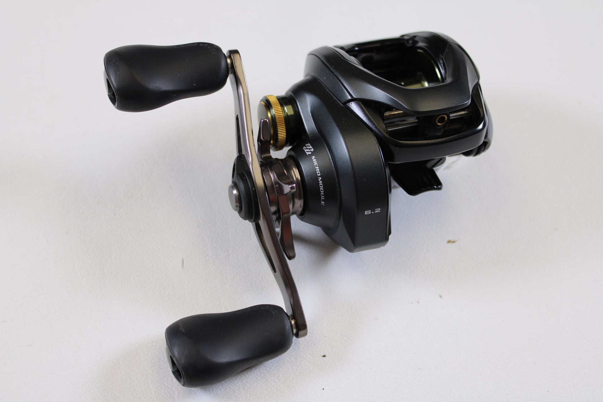 A Shimano Curado 200 K CU200K 6.2:1 RH used casting reel in excellent condition, with black finish, metallic accents, dual rubber handles, and a visible 6.2:1 gear ratio label rests on a white surface. Brand: Shimano.