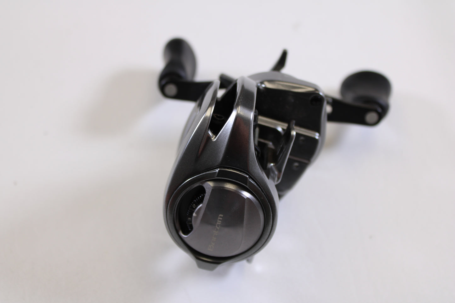 A close-up of a Shimano Bantam MGL BANTAMMGL151XG 8.1:1 LH Casting Reel in excellent used condition, featuring dual handles and adjustment knobs—ideal for your upgrade via our Rod and Reel Trade-In Program.