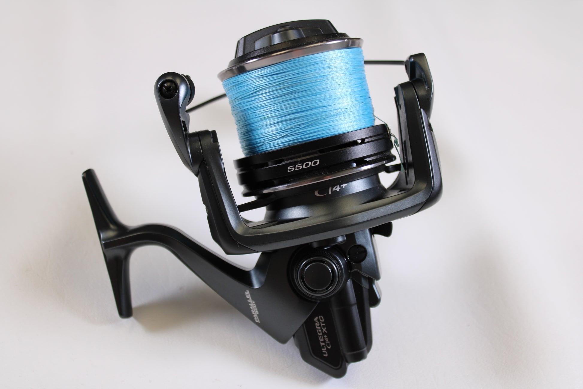 A close-up of the Shimano Ultegra CI4+ ULTCI45500XTC 5.3:1 Spinning Reel in excellent used condition with blue fishing line, set against a white background—ideal for quality gear hunters using our trade-in program.