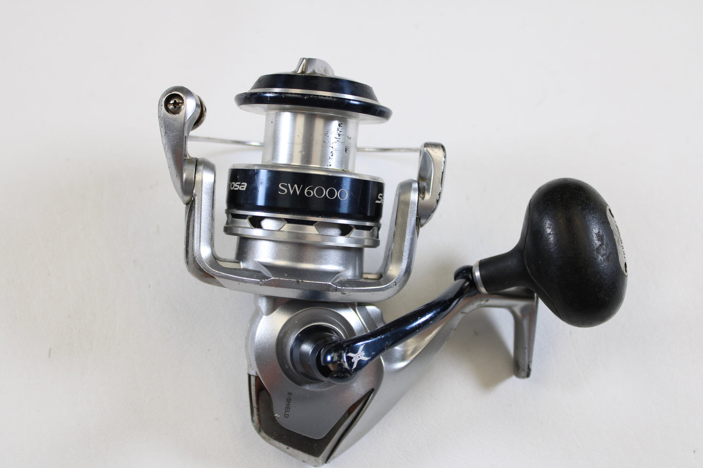 A used Shimano Saragosa SW A SRG6000SWAHG 5.7:1 spinning reel in good condition is shown on a white background. Perfect for anglers upgrading through our Rod and Reel Trade-In Program, it features a large handle and fishing line spool.