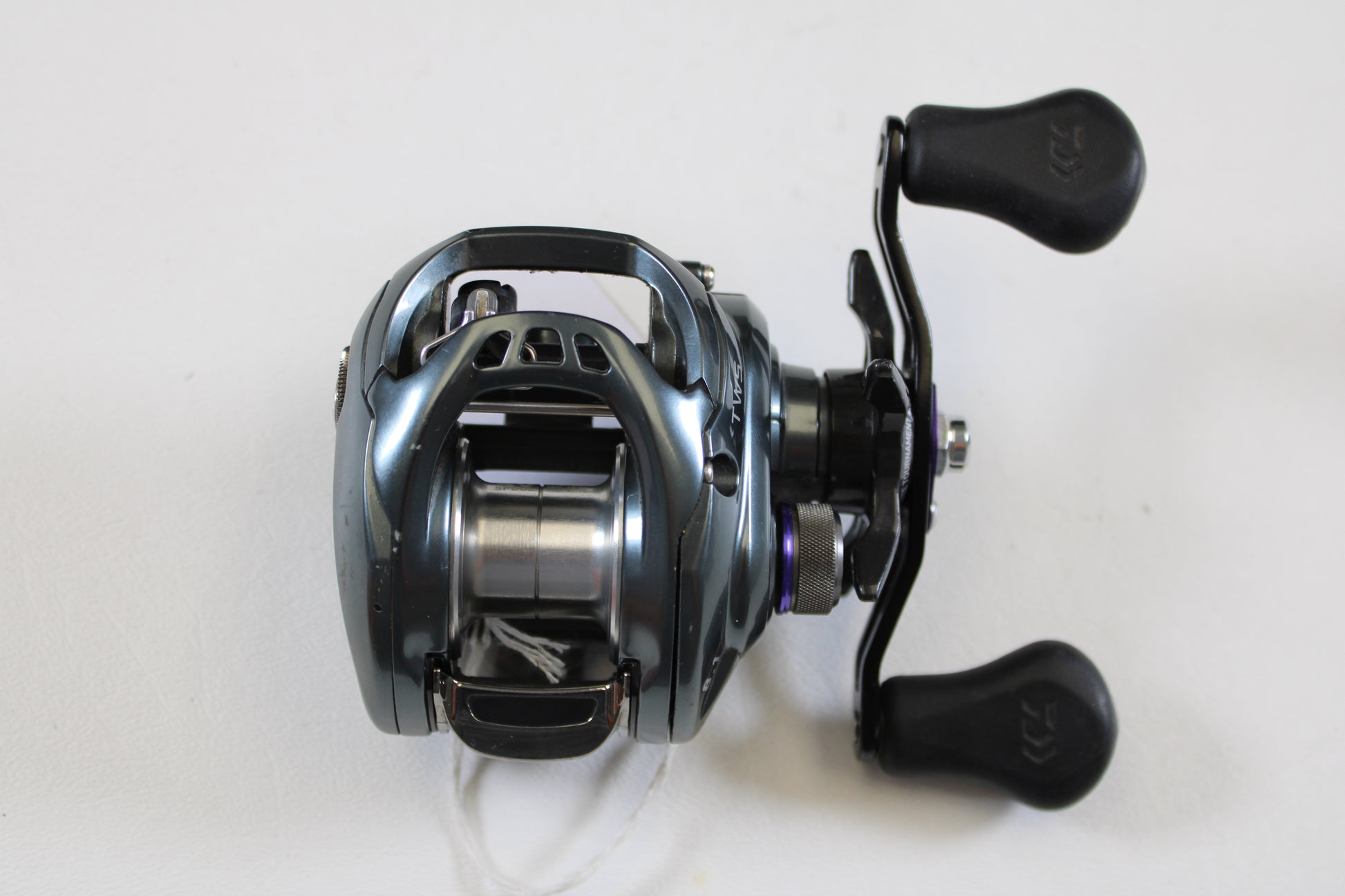 A used Daiwa Tatula SV TW TTUSV103XS 8.1:1 RH casting reel in good condition, with a metallic silver-blue finish and two black handles, ideal for our rod and reel trade-in program. Brand: Daiwa.