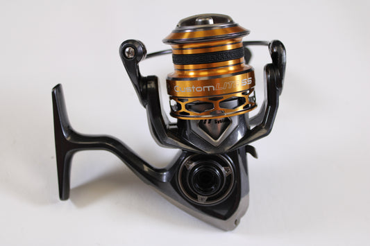 A close-up of a Lew's Custom Lite SS CLSS200 6.2:1 used spinning reel in black and orange, fair condition and missing handle nut, on a white background—ideal for trade-in and store credit through our Rod and Reel Trade-In Program.
