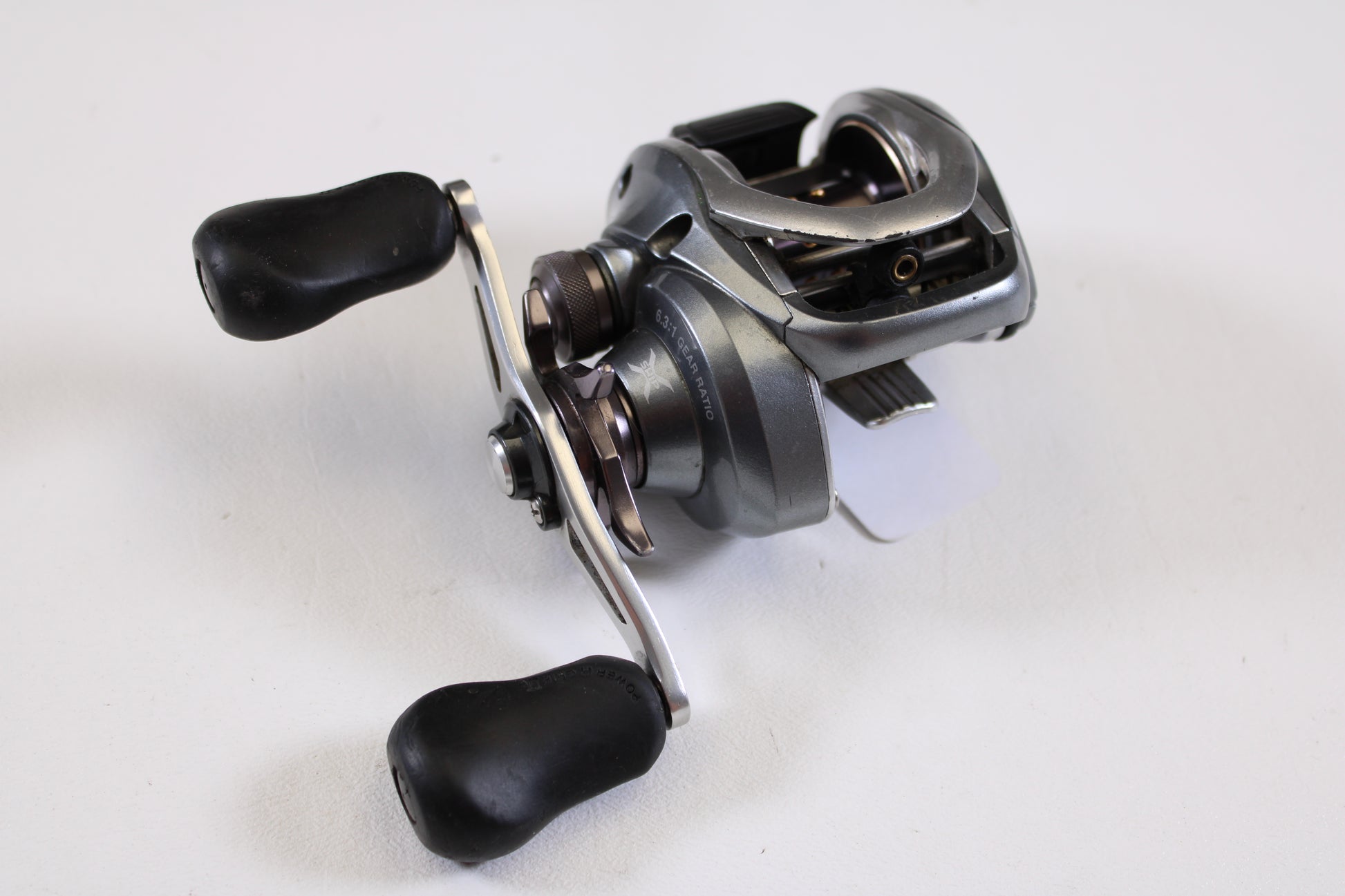 A close-up of a Shimano Curado I CU200I 6.3:1 RH used casting reel in good condition, featuring black handles and shown on a white surface—ideal for anglers seeking reliable, pre-owned Shimano fishing gear.