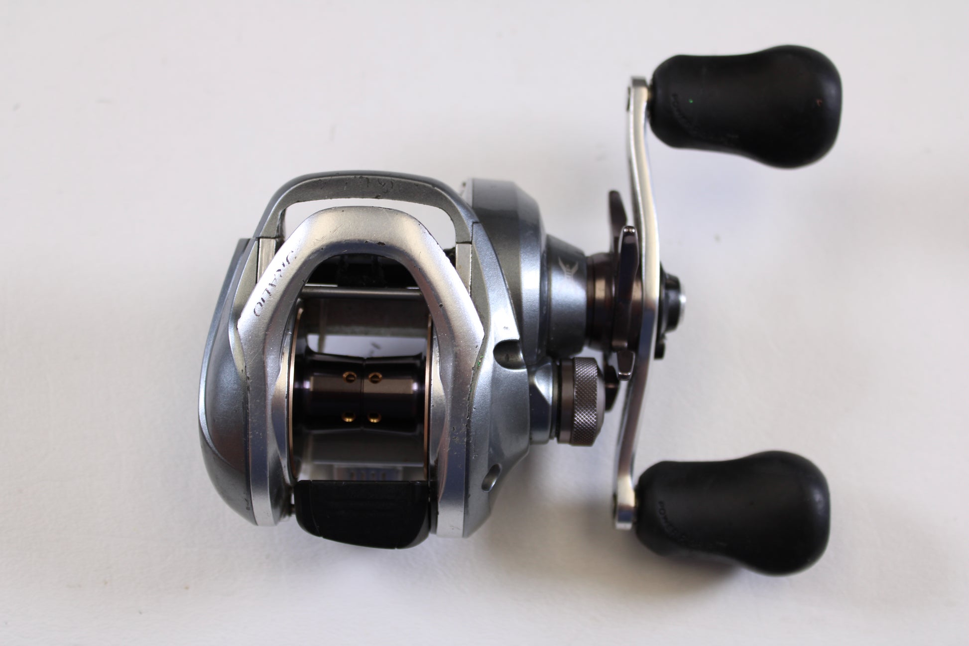 The Shimano Curado I CU200I 6.3:1 RH used casting reel in good condition features a silver and black design with dual black handles—ideal for your fishing gear trade-in or earning store credit.