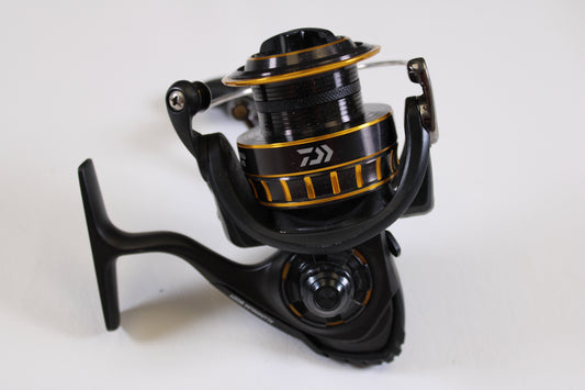 A close-up of a Daiwa BG BG3000 5.6:1 used spinning reel in excellent condition, featuring black and gold metallic details and a handle, displayed on a white background—ideal for our rod and reel trade-in program.