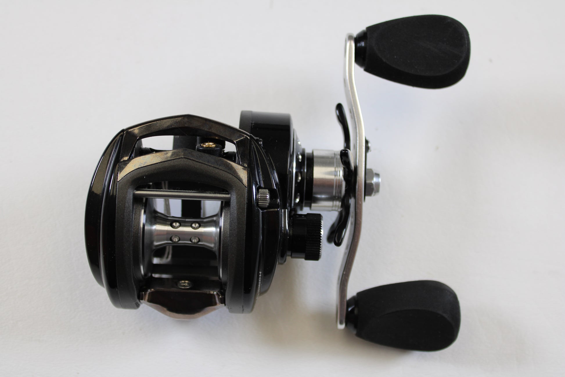 A close-up of an Abu Garcia Revo Winch Gen 3 RVO3 WNCH 5.4:1 RH—Used Casting Reel in Excellent Condition, featuring two handles and a spool on a white surface—ideal for our rod and reel trade-in program for store credit.