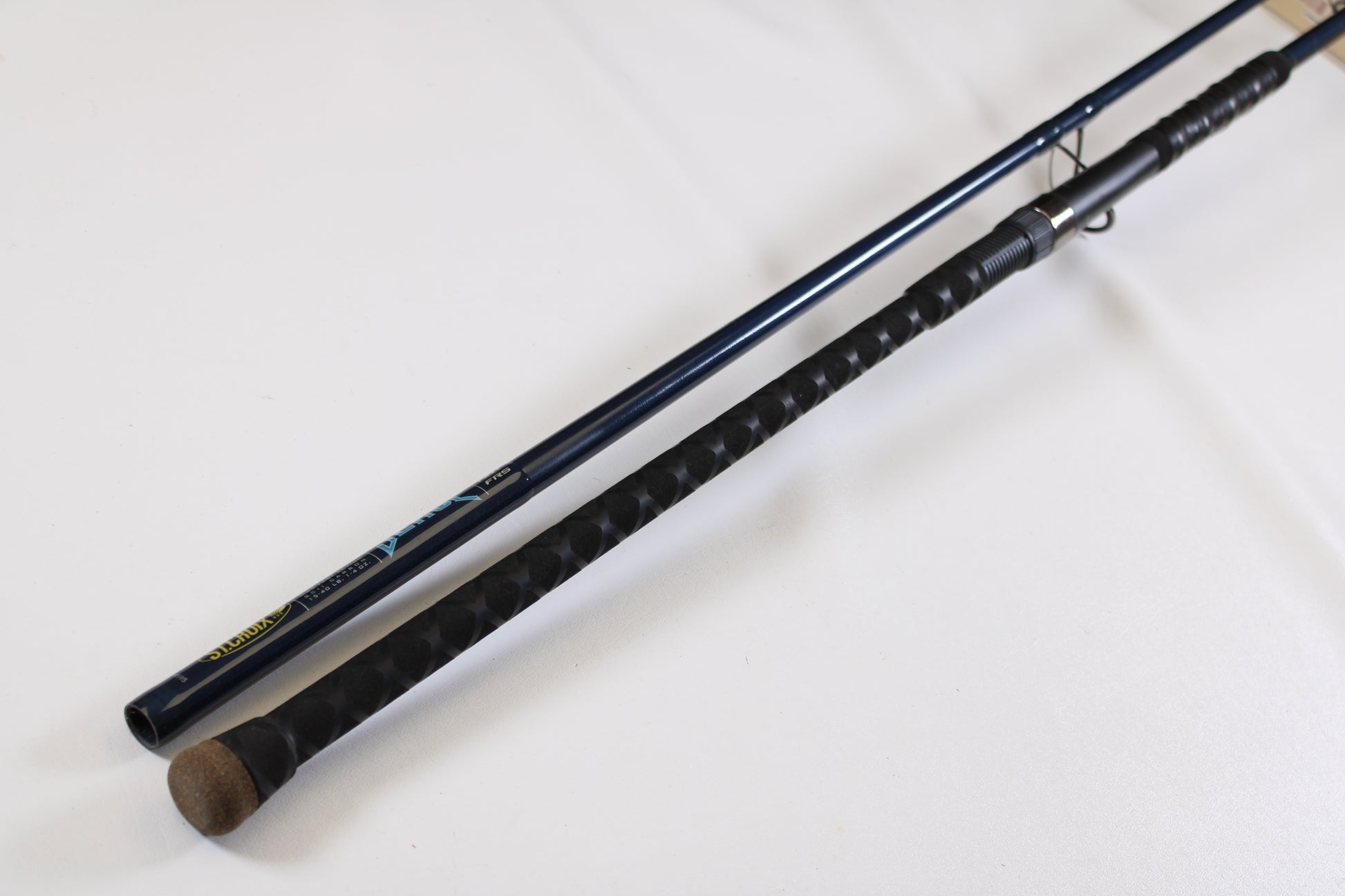 A close-up of two fishing rod handles on a white surface, including a St. Croix Seage SES90MMF2 9'0" Medium 2 Piece Used Spinning Rod—excellent condition, ideal for exchange in the Rod and Reel Trade-In Program to earn store credit.
