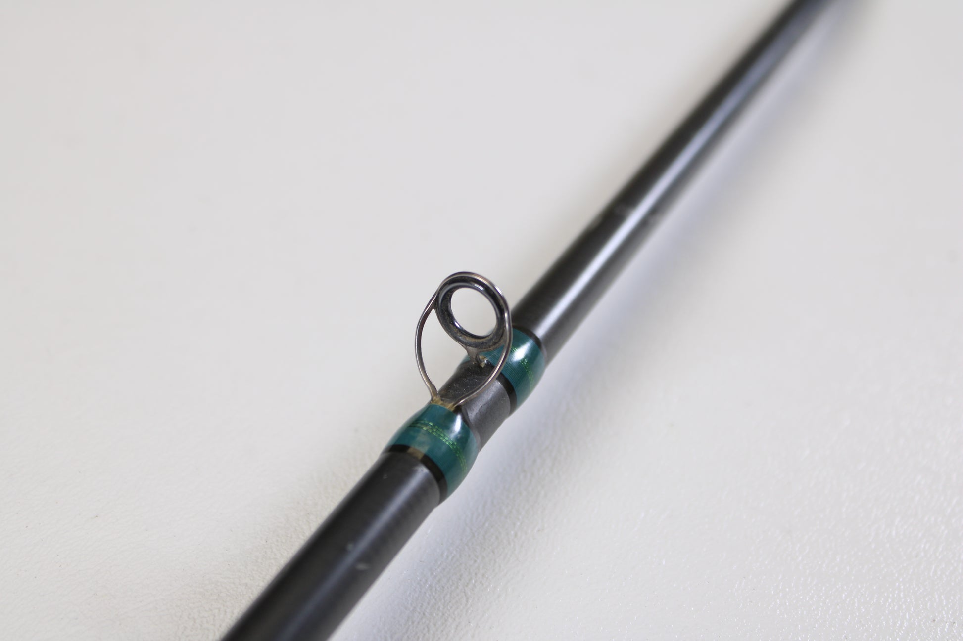 A close-up of a G. Loomis NRX 893c JWR 7'5" Medium Heavy Used Casting Rod in very good condition, highlighting a black line guide with teal thread, on a white background—ideal for our Rod and Reel Trade-In Program.