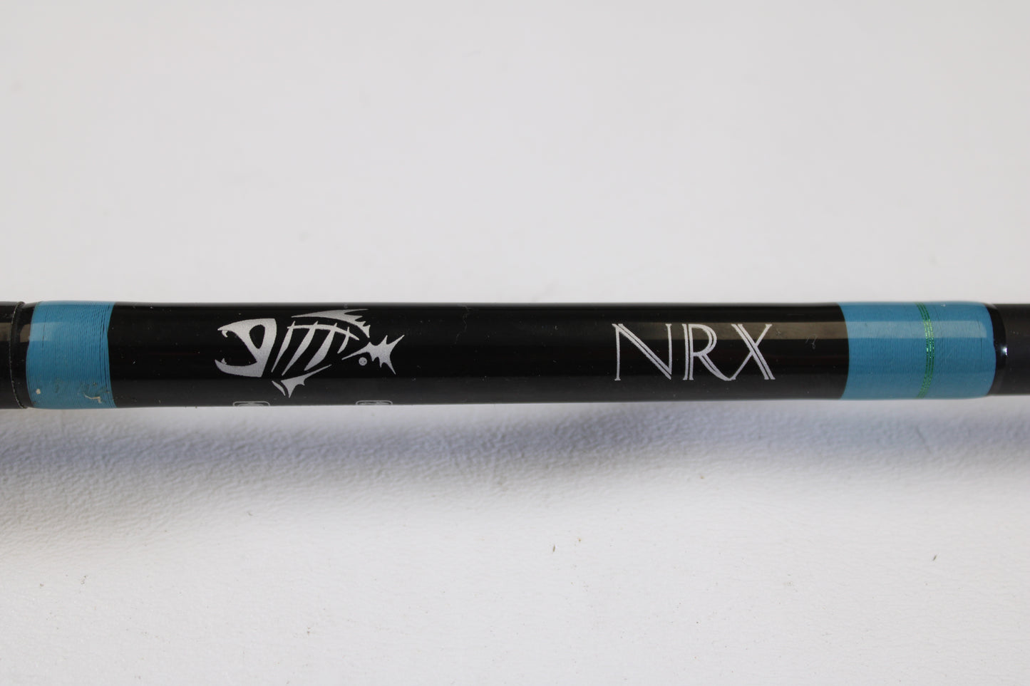 A close-up of the G. Loomis NRX 894c JWR 7'5" Heavy Used Casting Rod in excellent condition, featuring a black finish with a white fish skeleton logo and "NRX" lettering—ideal for those seeking top-quality used rods from G. Loomis.