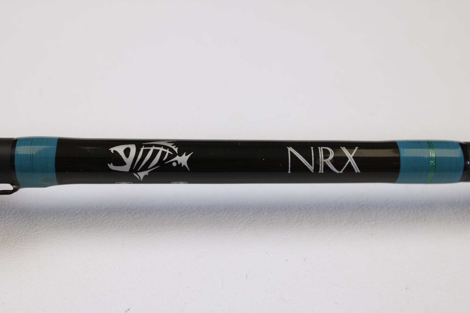 A close-up of the G. Loomis NRX 873c CRR 7'3" Medium Heavy used casting rod in excellent condition, featuring a black finish, white fish skeleton graphic, "NRX" text, and blue bands—eligible for our rod and reel trade-in program.