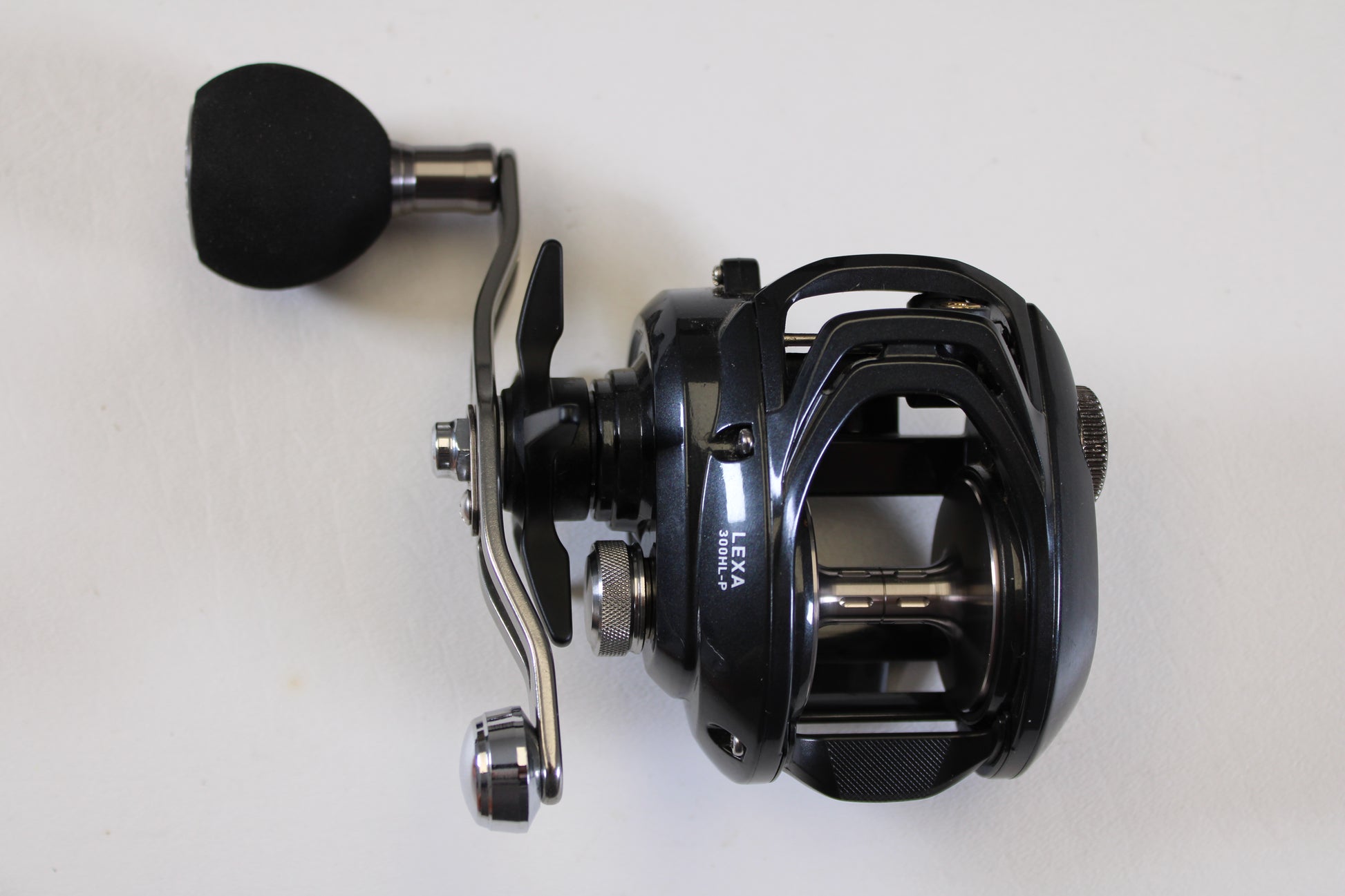 A close-up of the Daiwa Lexa 300 LX 300HL-P 7.4:1 LH Used Casting Reel in excellent condition, with a large padded handle, set against a plain white background—ideal for upgrades or our Rod and Reel Trade-In Program.
